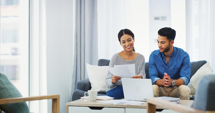 Photo documents laptop and portfolio with couple on sofa in home living room for bank payment accounting finance or refund with man and woman in apartment to review loan mortgage or tax on computer