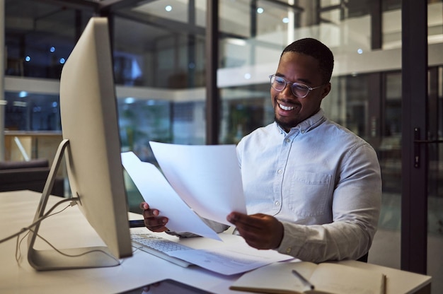 Documents night and computer with a businessman working at his desk late in the office Paperwork finance and tax with a male employee at work for overtime on a deadline while reading a report