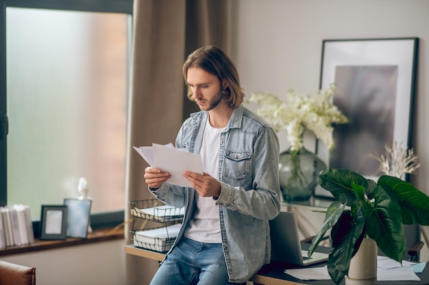 Documents. Young man in jeans shirt holding papers