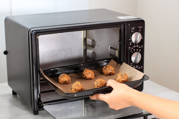 Doe geschept rauw koekjesdeeg van chocoladekoekjes in de oven. Koekjesdeeg in zwarte bak klaar om te bakken. Geselecteerde focus op vrouwelijke bakkershand