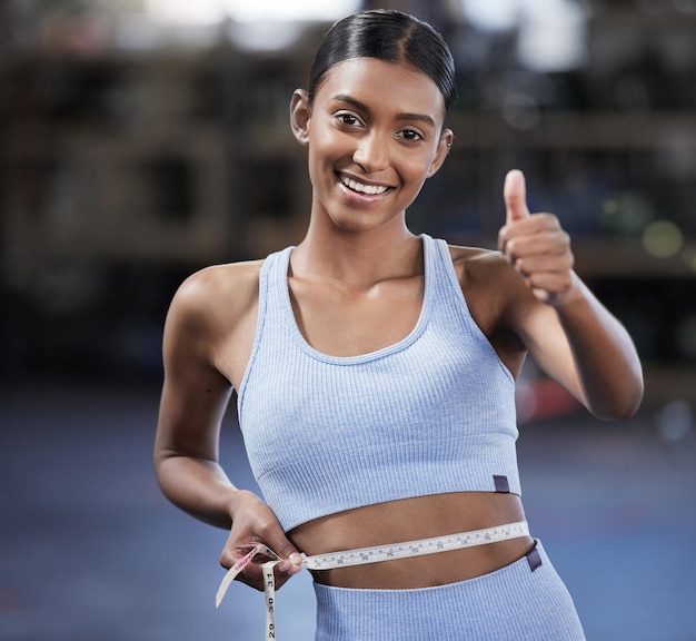 Doe je best en de resultaten laten zien Portret van een sportieve jonge vrouw die haar duimen opsteekt terwijl ze haar taille meet in een sportschool