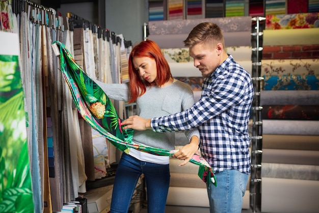 Doek aanraken. Paar kiezen voor textiel in woondecoratie winkel, winkel. Maken van interieurontwerp tijdens quarantaine. Gelukkige man en vrouw, jong gezin ziet er dromerig uit, vrolijk materiaal kiezen.