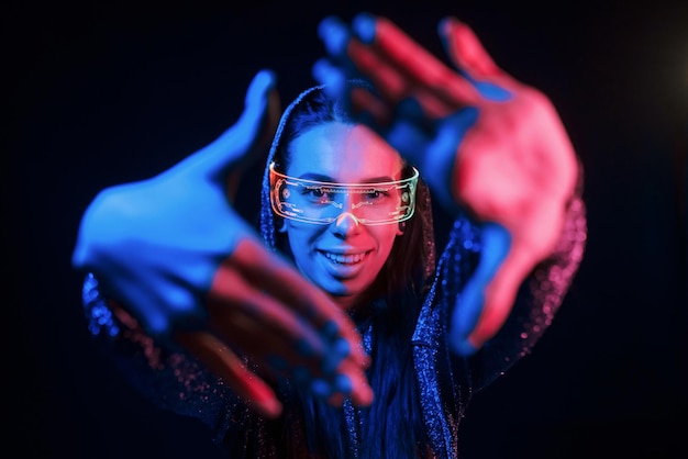 Does gestures by hands Portrait of young girl that is in eyeglasses in blue neon lighting