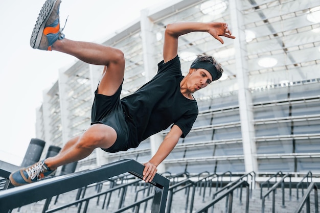 Does parkour Young man in sportive clothes have workout outdoors at daytime