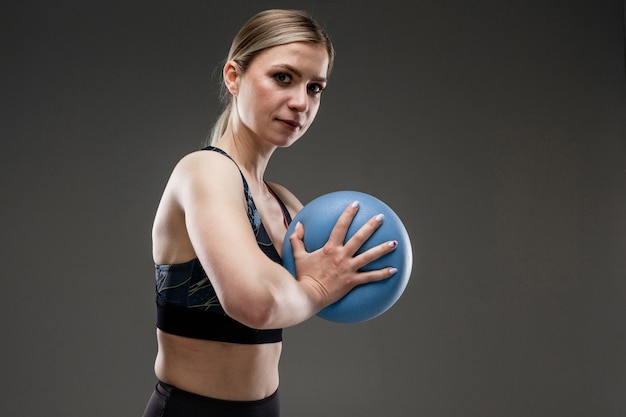 Doet het sport Kaukasische meisje met slank cijfer oefeningen met blauwe bal die op zwarte achtergrond wordt geïsoleerd