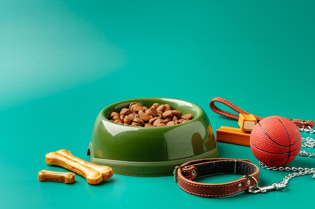 Dog dry food in bowl toy ball and leash on green background