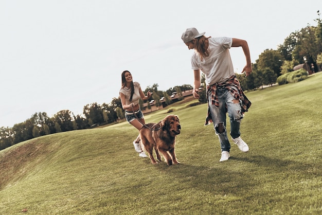 Il cane fa parte della loro famiglia. tutta la lunghezza della giovane coppia moderna che gioca con il proprio cane mentre trascorre del tempo spensierato nel parco