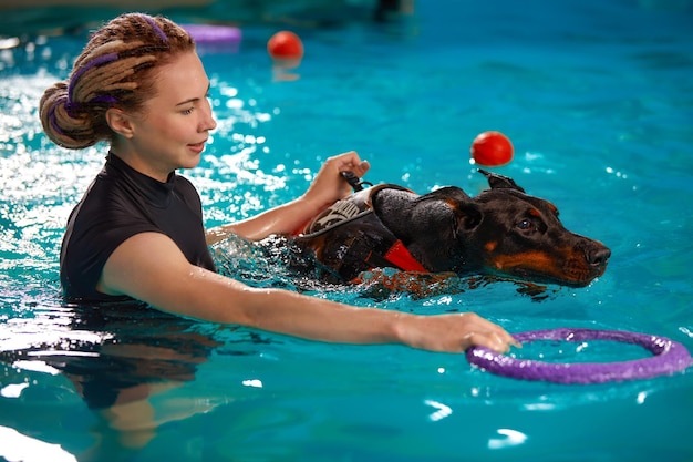 Dog in life jacket swim in the swimming pool with coach pet\
rehabilitation recovery training prevention for hydrotherapy pet\
health care