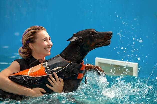 Dog in life jacket swim in the swimming pool with coach pet rehabilitation recovery training