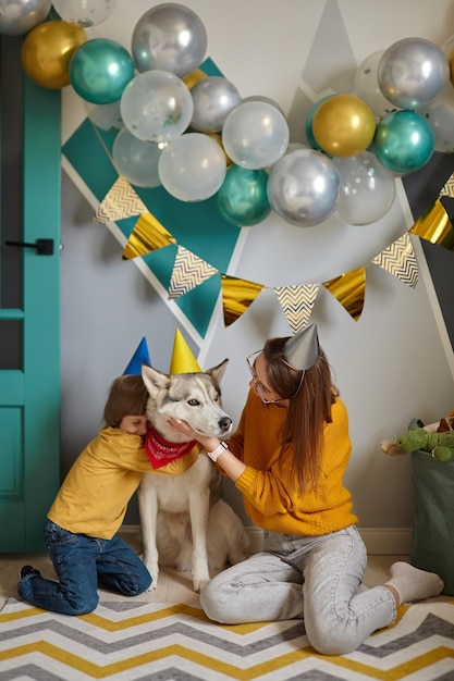 개 애완 동물 생일 가족 엄마와 아이는 생일 축하를 축하하는 개를 안아줍니다.