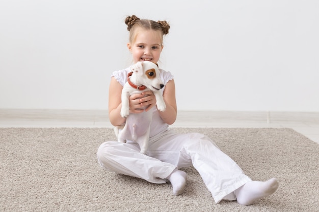 Concetto di cani, bambini e animali domestici - bambina seduta sul pavimento con un cucciolo carino.