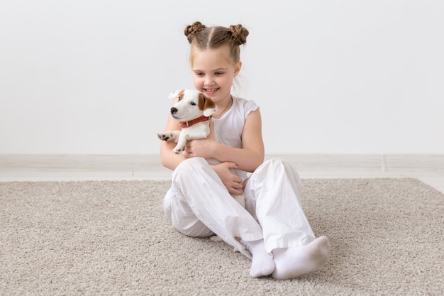 Dogs, children and pets concept - little child girl sitting on the floor with cute puppy.