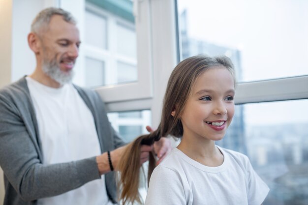 Doing hair. A gray-haired dad doing hair to his daughter