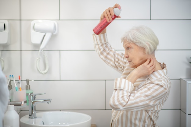 Doing hair. Gray-haired woman in pajama doing hair in the bathroom