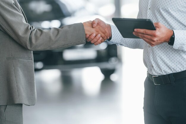 Photo doing handshake man in formal wear helping customer with choice of the automobile