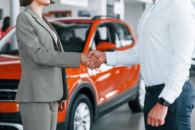 Photo doing handshake man in formal wear helping customer with choice of the automobile