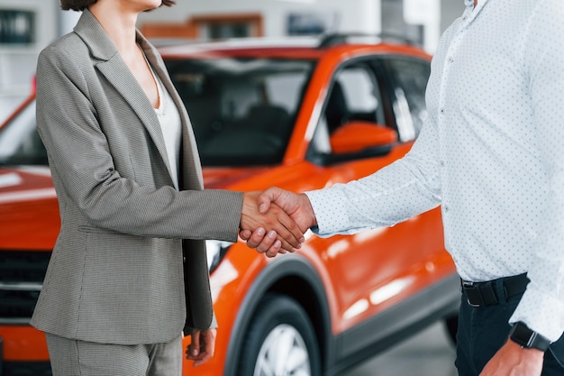 Photo doing handshake man in formal wear helping customer with choice of the automobile