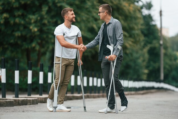 Фото Делая рукопожатие двое мужчин с костылями на улице на дороге