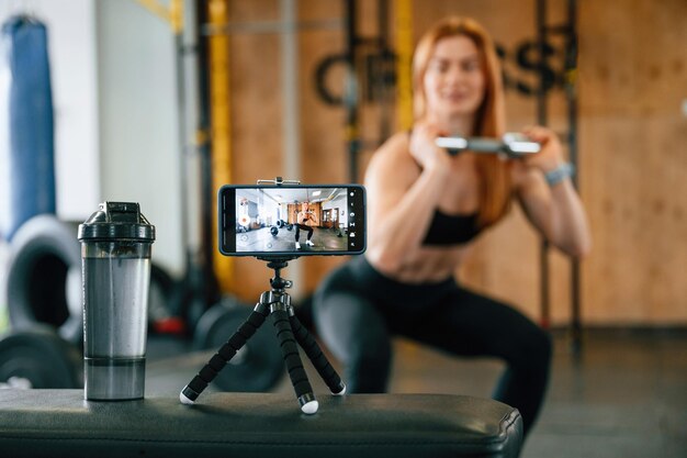 Foto fare squat girare video con lo smartphone bella donna forte è in palestra