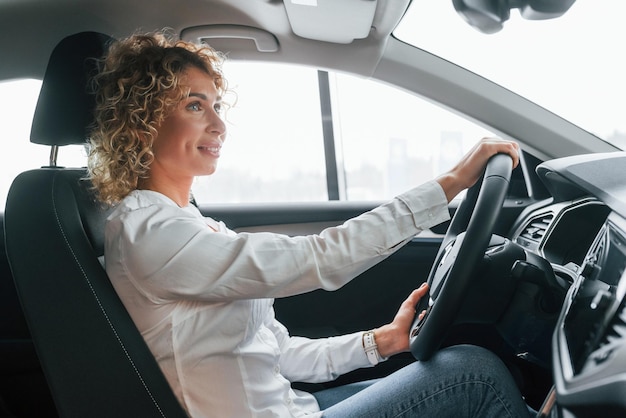 Doing test drive Woman with curly blonde hair is in autosalon