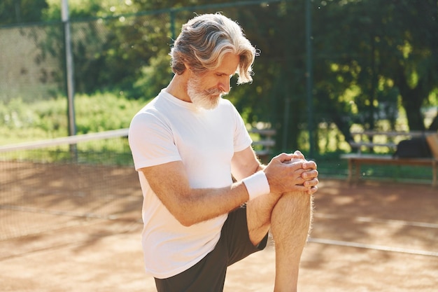 Doing warm up exercises Senior modern stylish man outdoors on the sportive field at daytime