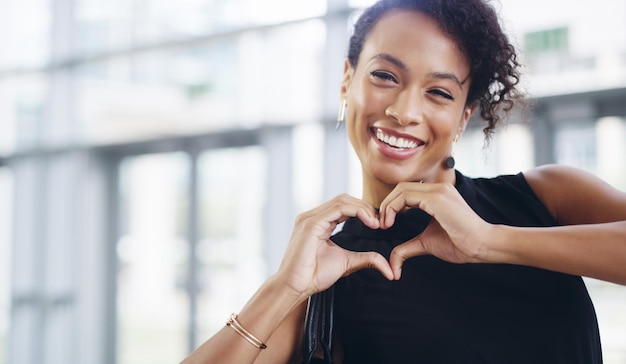 Doing what I love and loving what I do Cropped shot of a young businesswoman showing a heart sign while walking through a modern office