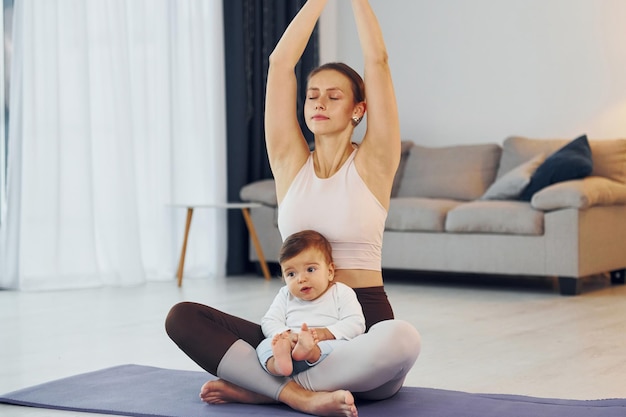 Doing yoga exercises mother with her little daughter is at home\
together