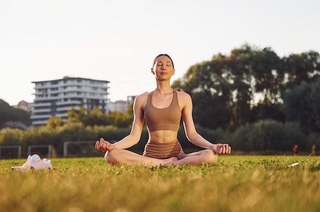 Doing yoga exercises Young woman in yoga clothes is outdoors on the field