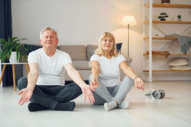 Doing yoga senior man and woman is together at home