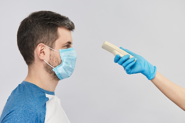 Dokter arm in blauwe gloed meet de temperatuur van het lichaam van de man in sterle masker met elektrothermometer