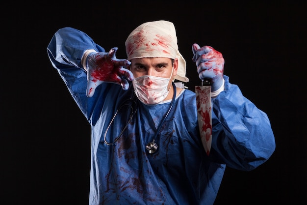 Dokter bedekt met bloed met masker op zijn gezicht voor halloween in studio. Portret van een dokter die eruitziet als een scewball.