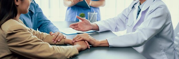 Dokter biedt medelijdende gezondheidszorgconsultatie terwijl jong echtpaar patiënt hand in hand elkaar troost na onvruchtbaar rapport Reproductieve en medische vruchtbaarheidsconsultatie Neoterisch