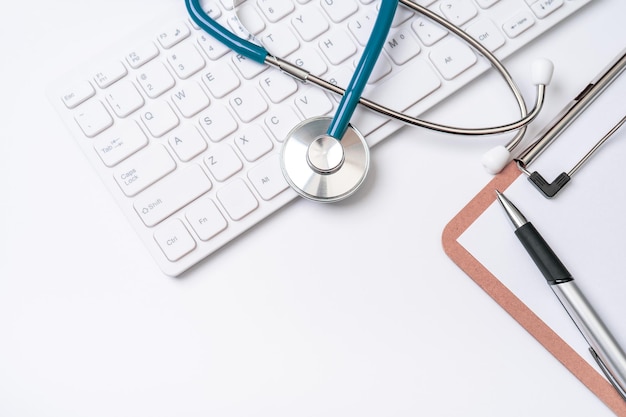 Dokter diagnosticeert concept stethoscoop op computertoetsenbord met medisch dossierkoffer en pen op witte werktafel Bovenaanzicht plat lag kopieerruimte
