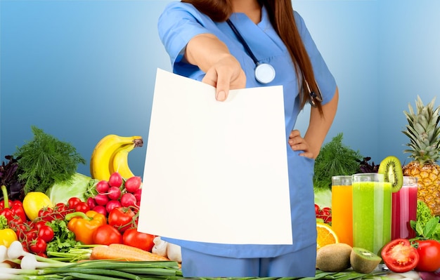 Foto dokter die blanco papier toont tegen een stapel groenten en fruit