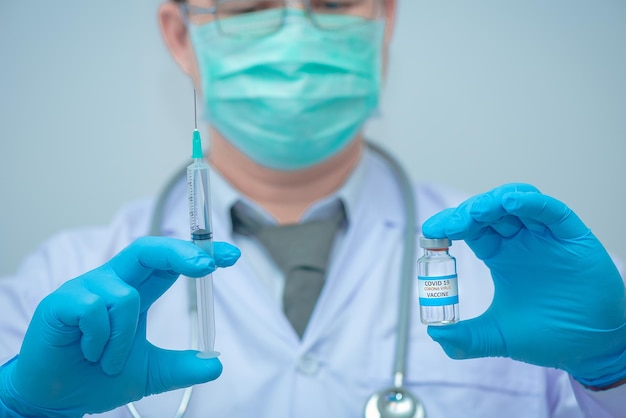 Dokter die blauwe handschoenen draagt, houdt virusmedicijn Corona en spuiten vast