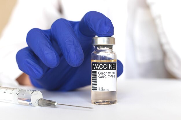 Dokter die COVID-19-vaccin presenteert, coronavirusbehandelingsconcept, hand in blauwe handschoenen houdt vaccinflacon, close-up, ziekenhuis- en medicijnachtergrondfoto