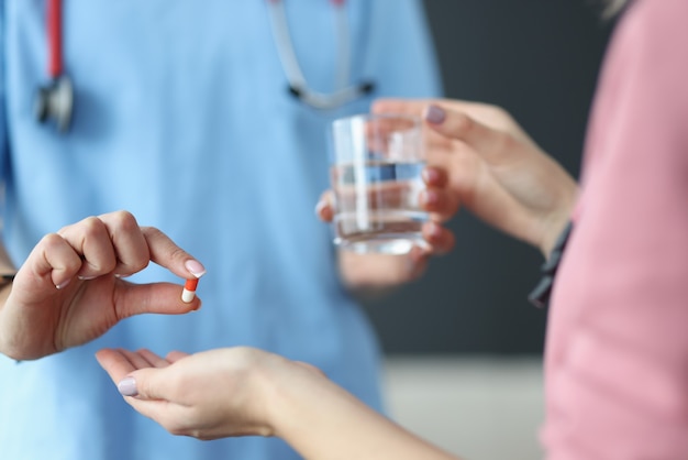 Dokter die geduldig glas water en capsule van geneeskunde in kliniekclose-up geeft