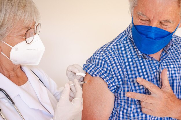 Dokter die injectie geeft aan senior blanke man, oud gepensioneerd, ontvangt derde booster van covid 19 vaccinmensen die masker dragen