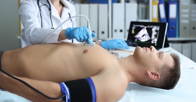 Dokter doet een hart-ultrasound aan een jonge mannelijke patiënt in de kliniek.