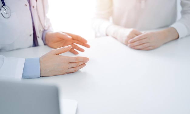 Dokter en patiënt bespreken actuele gezondheidsvragen terwijl ze dicht bij elkaar aan tafel in de kliniek zitten, alleen handen close-up. Geneeskunde concept