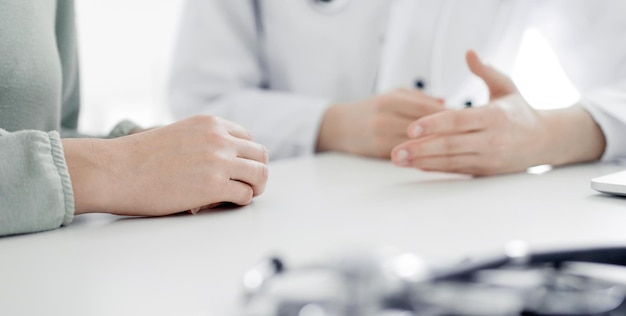 Dokter en patiënt bespreken het huidige gezondheidsonderzoek terwijl ze aan het bureau zitten in het kantoor van de kliniek, close-up.