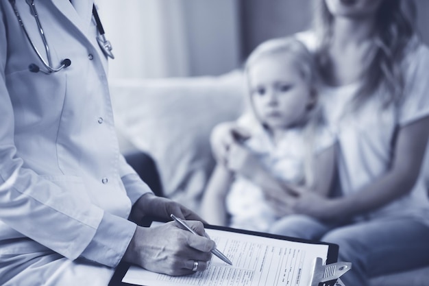 Foto dokter en patiënt. kinderarts die klembord gebruikt terwijl hij een klein meisje met haar moeder thuis onderzoekt. ziek en ongelukkig kind bij medisch onderzoek. geneeskunde concept.