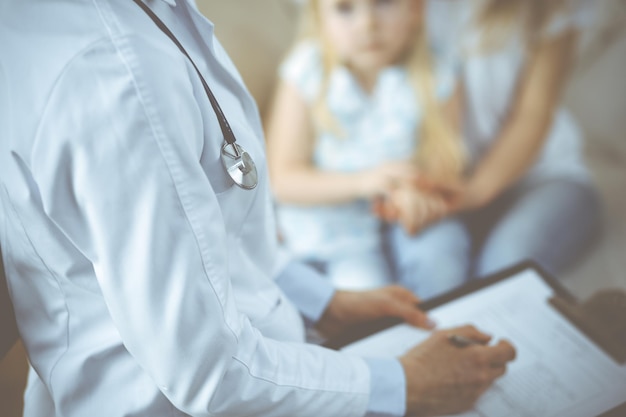 Dokter en patiënt. Kinderarts die klembord gebruikt terwijl hij een klein meisje met haar moeder thuis onderzoekt. Ziek en ongelukkig kind bij medisch onderzoek. Geneeskunde concept.