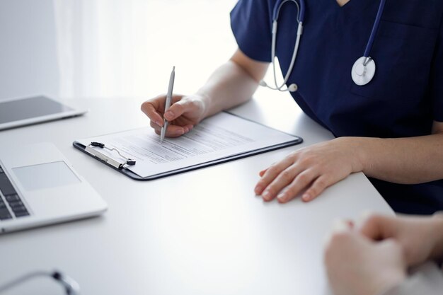 Dokter en patiënt zitten aan tafel in de kliniek terwijl ze iets bespreken. De focus ligt op de handen van de vrouwelijke arts, close-up. Geneeskunde concept