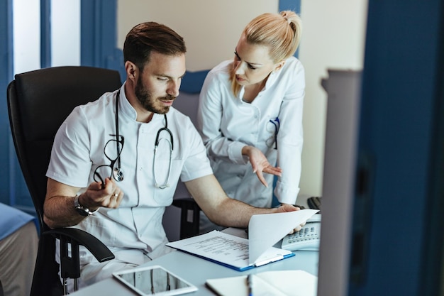 Foto dokter en zijn vrouwelijke collega's die medische rapporten doornemen en communiceren in de kliniek