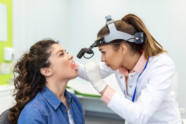 Dokter gebruikt inspectie spatula om de keel van de patiënt te onderzoeken HOO-arts doet keelonderzoek van een vrouwelijke patiënt die haar mond opende om de keel te controleren