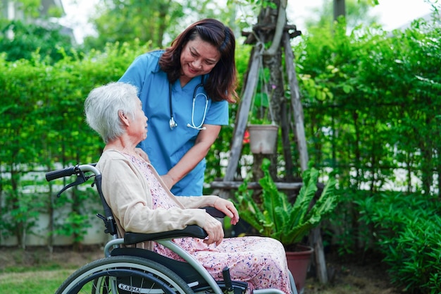 Dokter helpt Aziatische bejaarde vrouw met een handicap die op een rolstoel zit in het medische concept van het park