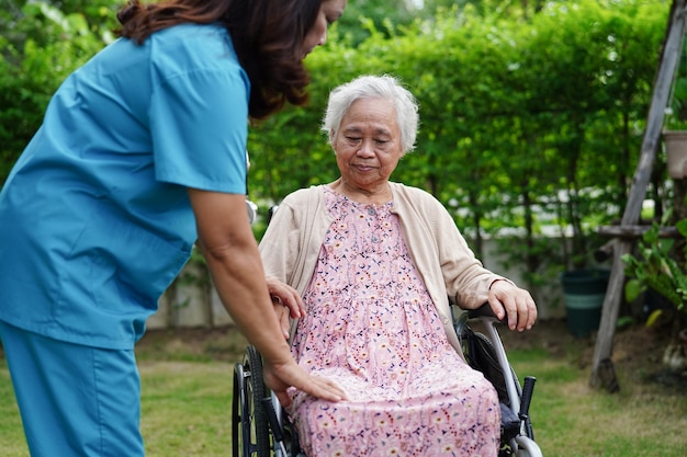 Dokter helpt Aziatische bejaarde vrouw met een handicap die op een rolstoel zit in het medische concept van het park