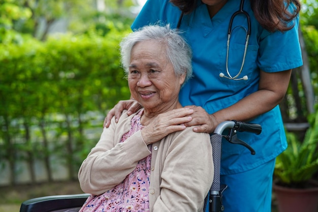 Dokter helpt Aziatische bejaarde vrouw met een handicap die op een rolstoel zit in het medische concept van het park