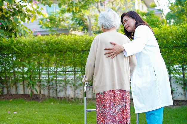 Dokter helpt Aziatische bejaarde vrouw met een handicap patiënt lopen met rollator in park medisch concept